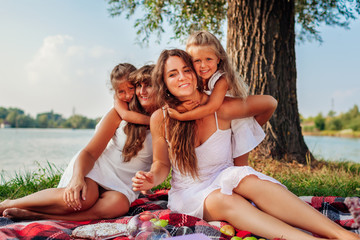 Mother's day. Family having picnic by spring river at sunset. Mother, grandmother and kids hugging laughing.
