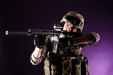 Soldier with gun is looking through the scope on violet background. Concept of war. Veterans,...
