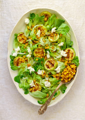 Delicious fresh lettuce salad with grilled zucchini, corn and soft goat cheese with spices and olive oil. Selective focus, top view