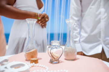 
Bride and groom pouring colorful different colored sands into the crystal vase close up during symbolic nautical decor destination wedding marriage ceremony on sandy beach in front of the ocean