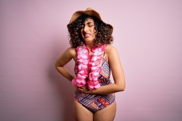 Young beautiful arab woman on vacation wearing swimsuit and hawaiian lei flowers with hand on stomach because nausea, painful disease feeling unwell. Ache concept.
