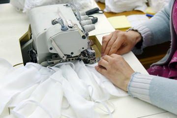 A woman sews gauze medical masks on a sewing machine, focus in the center.