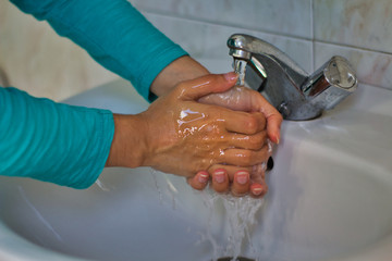 Woman wearing a blue shirt washing her hands with soap