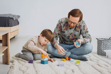 Father in glasses and adorable toddler son building wooden constructor tower.