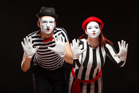 Portrait of man and woman mime artists performing, isolated on black background. Mimes in striped clothes pretending to be behind the glass