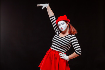 Portrait of female mime artist performing, isolated on black background. Woman raised her hand up....