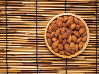 Top view almonds in wooden plate on bamboo mat with copy space.
