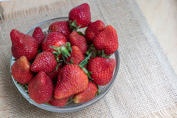 Strawberries in a glass plate on a wooden background. Strawberry season.