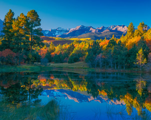 A pond surrounded by fall color reflects the trees and the Sneffels Range mountains in Ridgway, Colorado, USA.  This is in the San Juan Mountains.