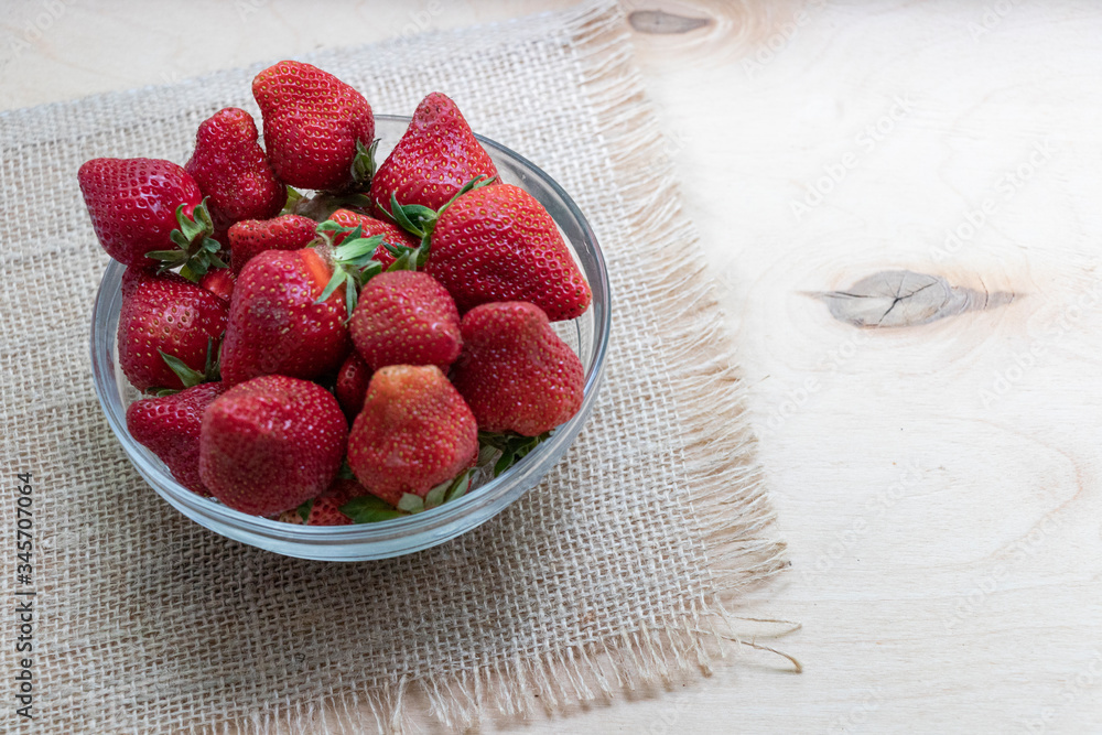 Wall mural strawberries in a glass plate on a wooden background. strawberry season.