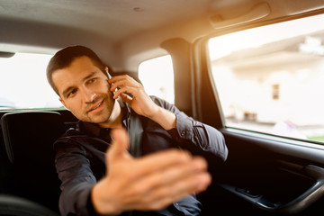 Busy businessman in a taxi. Multitasking concept. Passenger rides in the back seat and works simultaneously. Speaks on a smartphone and communicates with the driver