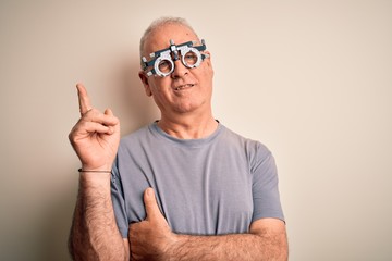 Naklejka premium Middle age hoary man controlling vision wearing optometry glasses over white background with a big smile on face, pointing with hand and finger to the side looking at the camera.