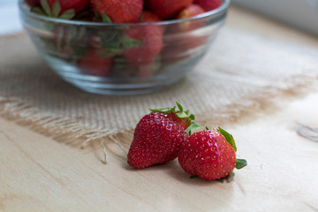 Strawberries in a glass plate on a wooden background. Strawberry season.