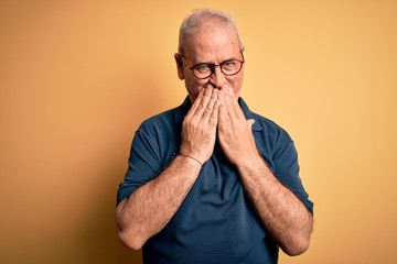 Middle age handsome hoary man wearing casual polo and glasses over yellow background laughing and embarrassed giggle covering mouth with hands, gossip and scandal concept