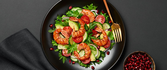 Shrimps salad, avocado, lettuce, cherry tomatoes. Homemade vegetarian shrimp salad. Seafood concept. Mixed leaves, grilled prawn shrimps in plate on black background, banner