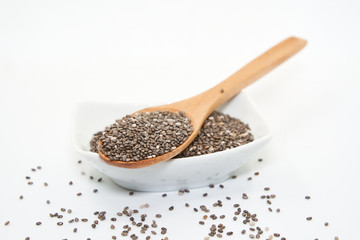 White porcelain bowl and wooden spoon with chia seeds, isolated on white background