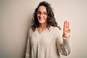 Beautiful woman with curly hair wearing casual sweater and glasses over white background showing and pointing up with fingers number three while smiling confident and happy.