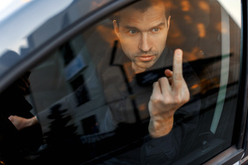 Angry man driving a car. Businessman shows middle finger in a car glass. A difficult situation on...