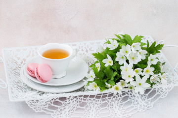 on a tray a cup of tea, macaroons and a bouquet of white flowers