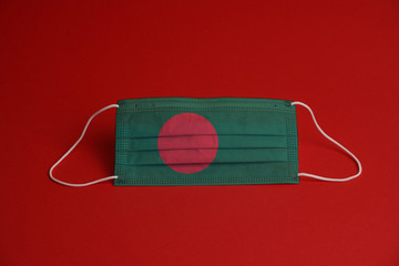 Coronavirus protective mask. Medical mask combined with the Bangladesh flag. Red background. Face mask protection against pollution, virus, flu. Healthcare and surgery concept.