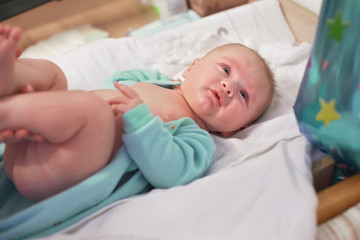 Infant baby boy laying on changing table, as his mother is preparing him, holding feet
