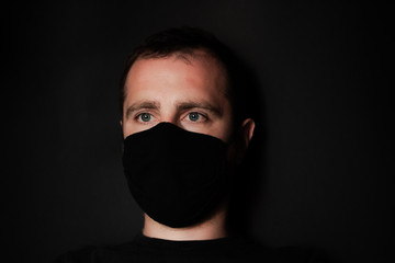 Young guy on black background in protective mask. A guy with black hair and a black face mask against
coronavirus disease. Problem of pandemic epidemic Coronovirus covid-19. Stay at home concept.