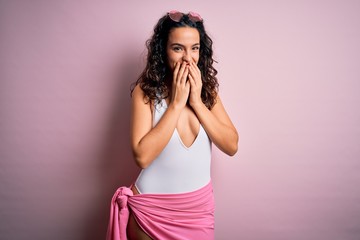 Beautiful woman with curly hair on vacation wearing white swimsuit over pink background laughing...