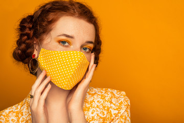Woman wearing stylish handmade protective face mask posing on orange background.  Model with...