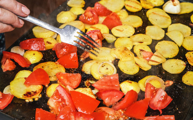 Tomatoes and potatoes cut to pieces grilled on electric grill, hand with fork moving vegetables