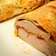 Close up de sanduíche folhado com muito recheio de mortadela, tomate seco, queijo e peito de peru.