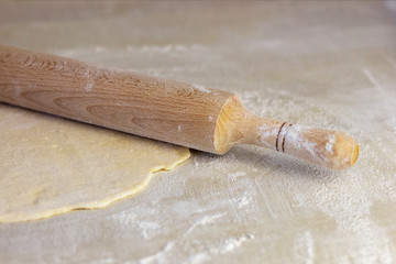 Rolling pin with dough on wooden worktop. Rolled out pizza dough.