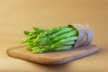 Bunch of fresh asparagus on a wooden board. Selective focus, brown blurred background.