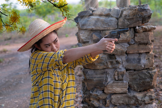 Portrait the farmer asea woman wearing a yellow shirt hand holding old revolver gun in the farm, Young girl with a handgun in garden