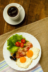On a wooden table is a plate with fried eggs and a cup of coffee.