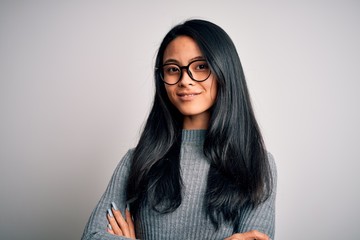 Young beautiful chinese woman wearing glasses and sweater over isolated white background happy face smiling with crossed arms looking at the camera. Positive person.