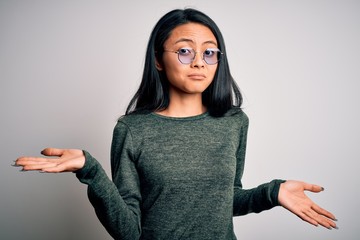 Young beautiful chinese woman wearing glasses and t-shirt over isolated white background clueless...
