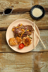 Soba buckwheat noodles with vegetables and chicken chop in Asian style with soy sauce on a wooden table.