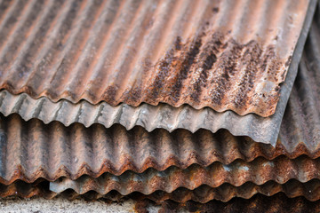 Sharp edges of the rusty metal sheets placed on the floor. Old aged weathered rusty galvanized corrugated iron sheet roof of abandoned mood. selective focus blur background. Vintage.