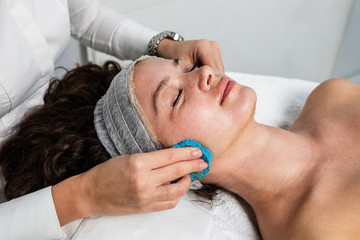 Fototapeta na wymiar Beautiful woman receiving natural green peel facial mask with rejuvenating effects in spa beauty salon.