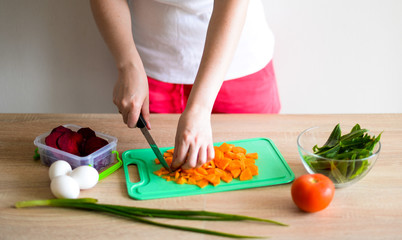 Obraz na płótnie Canvas A young woman cuts vegetables for soup in the kitchen: carrots, beets, onions, sorrel, tomato, eggs, May 4, 2020