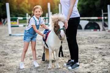 Obraz premium Cute little girl and her older sister enjoying with pony horse outdoors at ranch.