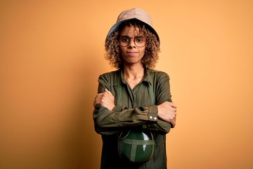 Young african american tourist woman on vacation wearing explorer hat and water canteen skeptic and...