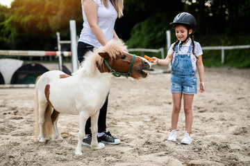 Cute little girl and her older sister enjoying with pony horse outdoors at ranch.