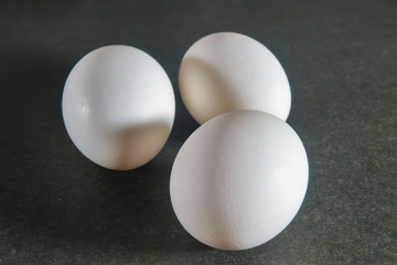 Three white chicken eggs on a dark background close-up.
