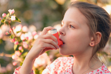 Little girl in the garden using an inhaler due to pollen allergy