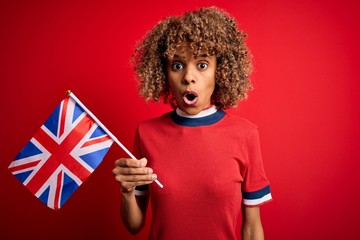 Young african american curly woman holding uk flag celebrating brexit referendum scared in shock with a surprise face, afraid and excited with fear expression