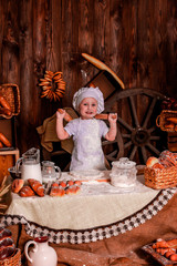  A young child in a chef's apron and hat plays the role of a baker.
The table is full of clutter. The mood is sublime. There are many ingredients and 
different things around. Concept for bakery.