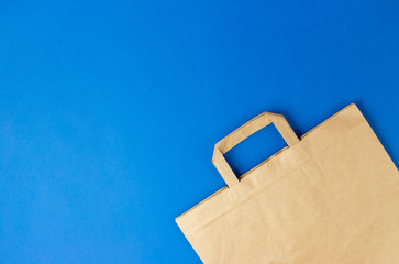 Craft brown paper bag with handles on blue background. Flat lay banner, top view, copy space, zero waste, plastic free items. Mockup eco package, delivery or online shopping concept