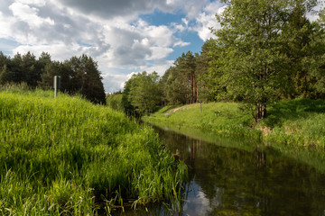 Fototapeta na wymiar A bend of a small river flowing between green, grassy hills and trees on a warm spring day