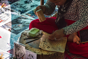 A local, cambodian woman is sitting and preparing colorful, traditional handcrafted pictures with...